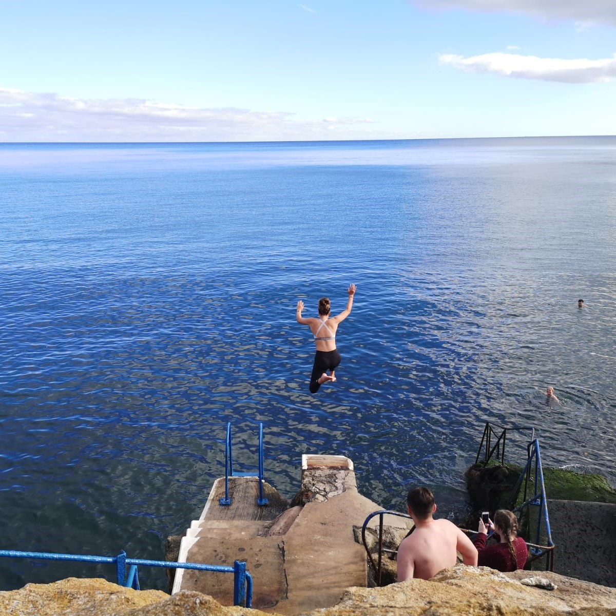 Young woman jumps into the sea from a high pier.